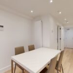 Property for sale A modern, minimalistic dining area with a white table and four beige chairs, set within a high yield London property. Light wood flooring and white walls create an airy space that connects to a hallway and partially visible kitchen appliances. Presented by Palace Auctions