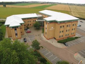 Property for sale Aerial view of a modern, three-story office building with a white roof in Wath-Upon-Dearne, ideal as a Rotherham investment property. Several cars are parked near the entrance, and trees border the property. Presented by Palace Auctions