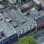 Property for sale Aerial view of a row of buildings along Cricklewood Broadway, with Crusader House, 283 Cricklewood Broadway, London NW2 6NX outlined in yellow. Rooftops, parked cars, and trees are visible nearby. Presented by Palace Auctions