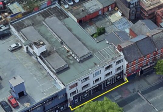 Property for sale Aerial view of a row of buildings along Cricklewood Broadway, with Crusader House, 283 Cricklewood Broadway, London NW2 6NX outlined in yellow. Rooftops, parked cars, and trees are visible nearby. Presented by Palace Auctions