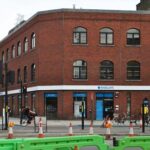 Property for sale A red-brick building on a city street corner houses a Barclays bank branch. Cyclists and pedestrians pass by, with green construction barriers and traffic lights framing this Whitechapel Road mixed-use development opportunity. Presented by Palace Auctions