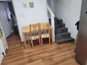 Property for sale A small wooden table with two chairs sits against a white wall near a carpeted staircase in this Abbey Lane Investment Property. Two framed pictures hang above the table, with wood flooring and a partially visible refrigerator on the right. Presented by Palace Auctions
