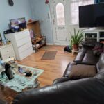 Property for sale A cozy living room in an investment property Leicester, featuring brown leather sofas, a glass coffee table, two TVs, a white dresser, houseplants, and wooden floors. The tidy space offers comfort and style—ideal for 2-bed houses Leicester investors. Presented by Palace Auctions