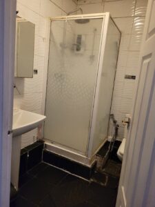 Property for sale A small bathroom in this Abbey Lane Investment Property features a black tiled floor, white sink, mirror, and a glass shower enclosure with frosted patterns. A toilet sits next to the shower, and the door is slightly open. Presented by Palace Auctions
