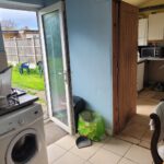 Property for sale A small kitchen in one of the 2-bed houses Leicester offers, with a washing machine, dishes drying on the counter, and a door open to a grassy backyard. White cabinets, microwave, and chairs are visible, plus a green recycling bag and broom near the door. Presented by Palace Auctions
