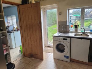 Property for sale A bright kitchen in one of the 2-bed houses Leicester offers, featuring a washing machine under the counter, stainless steel sink, dish rack, potted plants on the windowsill, and doors leading to a utility room and green garden. Presented by Palace Auctions