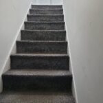 Property for sale A carpeted staircase with dark gray steps leads up between white walls to a closed white door at the top, creating an inviting entrance to this Abbey Lane investment property—an excellent split unit investment in Leicester. Presented by Palace Auctions