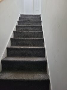 Property for sale A carpeted staircase with dark gray steps leads up between white walls to a closed white door at the top, creating an inviting entrance to this Abbey Lane investment property—an excellent split unit investment in Leicester. Presented by Palace Auctions
