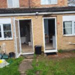 Property for sale A brick house with two open doors reveals a kitchen inside. The area is under construction with exposed wood. The garden features scattered items, grass, and a stone path—ideal for those seeking an Abbey Lane Investment Property in Leicester. Presented by Palace Auctions