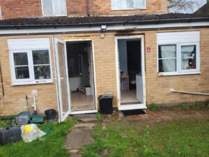 Property for sale A brick house with two open doors reveals a kitchen inside. The area is under construction with exposed wood. The garden features scattered items, grass, and a stone path—ideal for those seeking an Abbey Lane Investment Property in Leicester. Presented by Palace Auctions