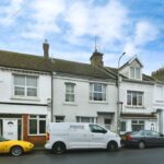 Property for sale A row of terraced houses with white facades sits beneath a cloudy sky. Parked in front are a yellow convertible, a white Morrison's Energy Services van, and a dark car—perfect South Road investment for those eyeing the Newhaven property auction. Presented by Palace Auctions