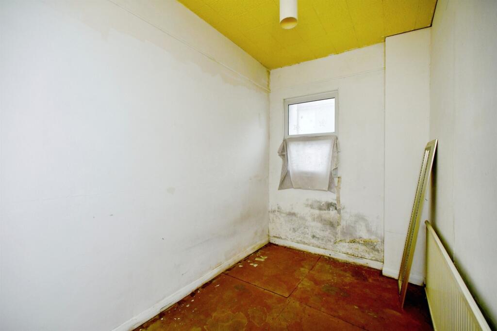 Property for sale A small, empty room in a 2-bed maisonette Newhaven, with stained white walls, yellow ceiling, brown floor, and mold near a window covered by a sheet. A radiator and large mirror lean against the right wall—ideal for investment or lease extension. Presented by Palace Auctions