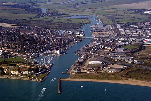 Property for sale Aerial view of Newhaven’s river estuary with boats, docks, industrial buildings, and a marina—surrounded by a coastal town, green fields, and cliffs—revealing the area’s investment potential for a 2-bed maisonette. Presented by Palace Auctions
