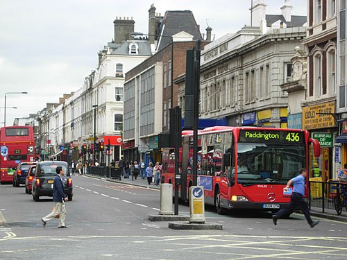 Property for sale A busy city street with red double-decker and single-decker buses, pedestrians crossing, and rows of shops with signs. The bus displays "436 Paddington" as its destination. Buildings have traditional architecture. Presented by Palace Auctions
