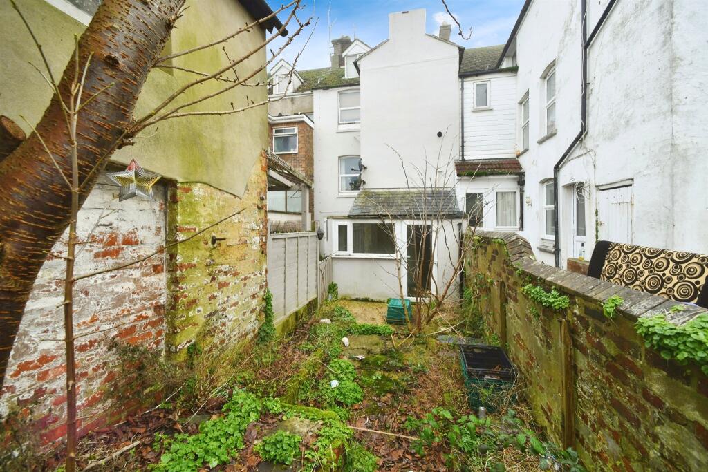 Property for sale Small, overgrown backyard with patchy grass, weeds, and mossy stone walls—ideal for a creative South Road investment. Surrounded by old white and brick houses; a bare tree and scattered items are visible. Presented by Palace Auctions
