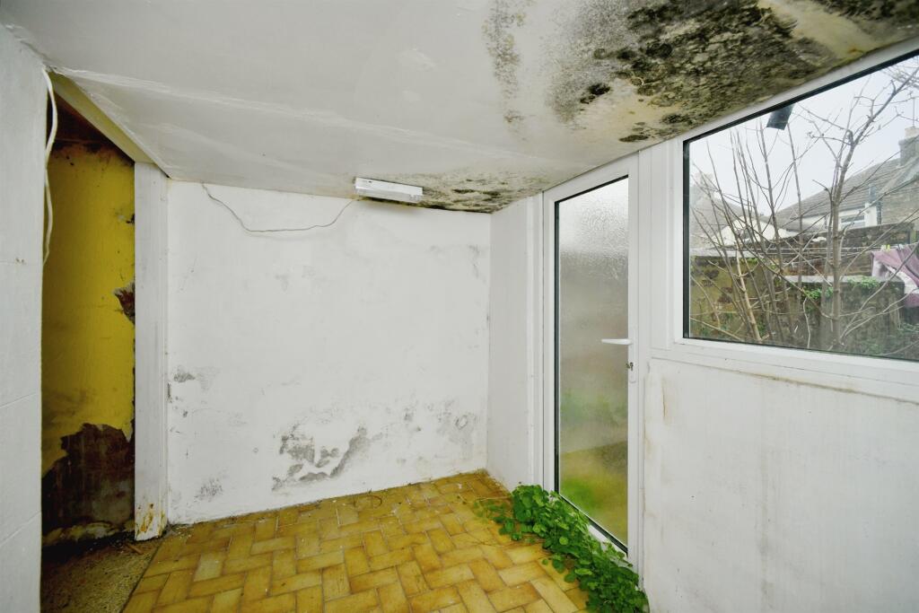 Property for sale Small, empty room with stained walls and mold on the ceiling in a 2-bed maisonette Newhaven. Patches of peeling paint, a glass door and window to the garden, and green plants growing inside along the floor by the door. Presented by Palace Auctions