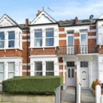 Property for sale A row of Victorian-style red brick terraced houses with white window frames and decorative trim, featuring small front gardens bordered by hedges and fences, includes a six-bed terrace London property under a blue sky. Presented by Palace Auctions