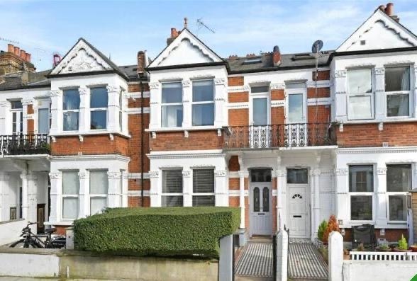 Property for sale A row of Victorian-style red brick terraced houses with white window frames and decorative trim, featuring small front gardens bordered by hedges and fences, includes a six-bed terrace London property under a blue sky. Presented by Palace Auctions