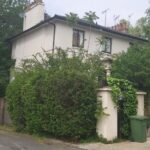 Property for sale A two-story house partially covered by green vines and trees stands at the corner of a quiet street on Greville Place NW6, with green and black bins by the entrance and a wooden fence running along the side. Presented by Palace Auctions