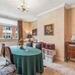 Property for sale A charming 3-bedroom apartment in Marylebone with a dining room featuring a green tablecloth-covered table, vintage decor, a chandelier, beige walls, framed art, and a large window with brown curtains—a lovely investment property in Marylebone. Presented by Palace Auctions