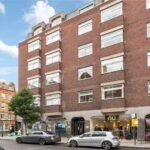 Property for sale A multi-story red brick building with large rectangular windows and shops at street level, including "nu" and "Cinnamon," sits in prime central London; ideal as an investment property Marylebone, with another historic building nearby. Presented by Palace Auctions