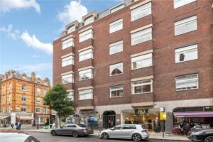 Property for sale A multi-story red brick building with large rectangular windows and shops at street level, including "nu" and "Cinnamon," sits in prime central London; ideal as an investment property Marylebone, with another historic building nearby. Presented by Palace Auctions
