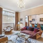 Property for sale A spacious living room in this 3-bedroom apartment Marylebone features beige walls, large window, colorful sofas and armchair, coffee table, chandelier, and dining area with a green-covered table—an inviting investment property Marylebone. Presented by Palace Auctions