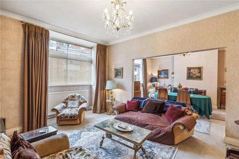 Property for sale A spacious living room in this 3-bedroom apartment Marylebone features beige walls, large window, colorful sofas and armchair, coffee table, chandelier, and dining area with a green-covered table—an inviting investment property Marylebone. Presented by Palace Auctions