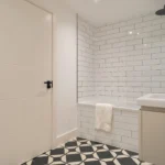 Property for sale Modern bathroom in one of the new build homes in Sheffield, featuring white subway tile walls, a bathtub with towel, black rainfall showerhead, geometric floor tiles, white door, and sleek towel rack. Presented by Palace Auctions