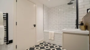 Property for sale Modern bathroom in one of the new build homes in Sheffield, featuring white subway tile walls, a bathtub with towel, black rainfall showerhead, geometric floor tiles, white door, and sleek towel rack. Presented by Palace Auctions