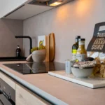 Property for sale A modern kitchen countertop, perfect for modern flats in Sheffield, with an electric stove, sink, olive oil, pasta, salt, a bowl, and a small potted plant on a white tray. Light wood cabinets add to the minimal decor. Presented by Palace Auctions