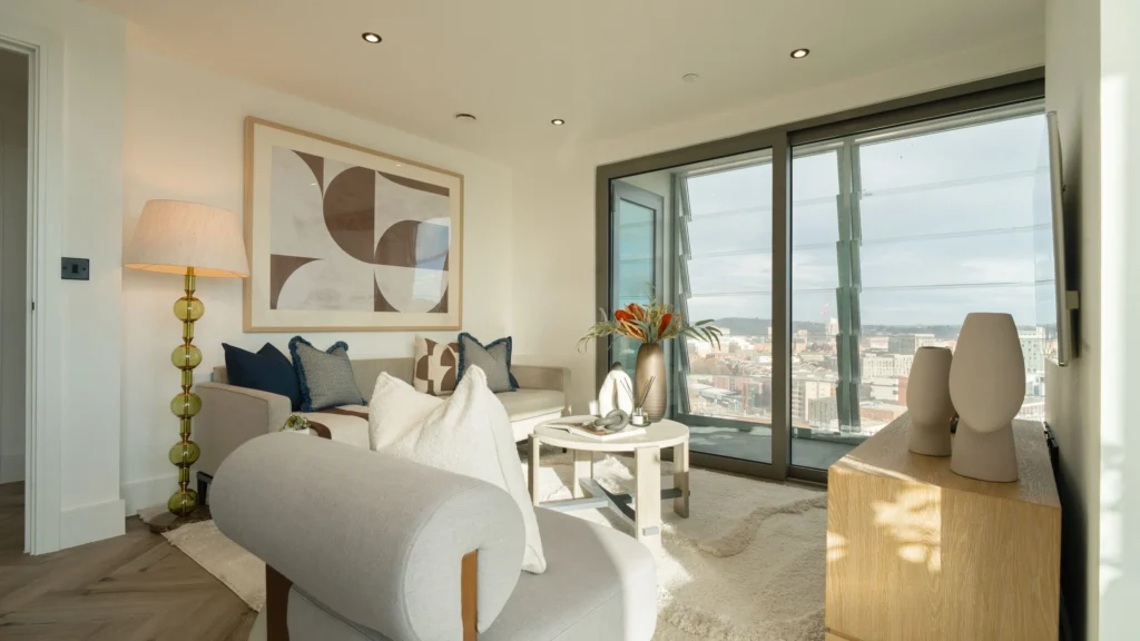 Property for sale A modern living room in Langford Tower Sheffield features light-colored furniture, abstract wall art, a floor lamp, and large glass doors opening to a balcony with a city view—ideal for those seeking stylish apartments for sale in Sheffield. Presented by Palace Auctions