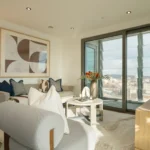 Property for sale A modern living room in Langford Tower Sheffield features light-colored furniture, abstract wall art, a floor lamp, and large glass doors opening to a balcony with a city view—ideal for those seeking stylish apartments for sale in Sheffield. Presented by Palace Auctions