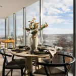 Property for sale Modern dining area with round table set for four, large vase with flowers, and floor-to-ceiling windows showcasing panoramic city views. Light wood floors and minimalistic décor enhance this bright space in Langford Tower Sheffield. Presented by Palace Auctions