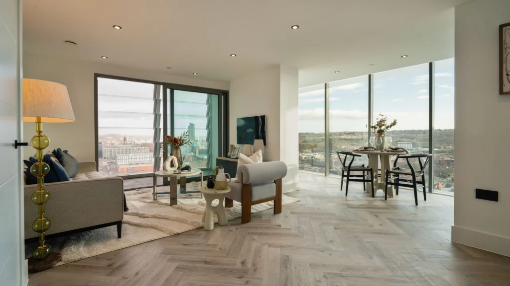 Property for sale Modern, bright apartment in Langford Tower Sheffield with large windows offering a city view, a cozy living area with sofas and a rug, a dining table with chairs, and neutral, stylish décor throughout. Presented by Palace Auctions