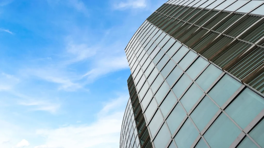 Property for sale A modern glass building with a curved design rises against a bright blue sky with wispy clouds—an impressive example of new build homes in Sheffield, featuring reflective windows arranged in a grid pattern. Presented by Palace Auctions