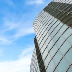 Property for sale A modern glass building with a curved design rises against a bright blue sky with wispy clouds—an impressive example of new build homes in Sheffield, featuring reflective windows arranged in a grid pattern. Presented by Palace Auctions