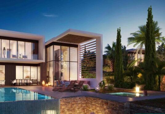 Property for sale Modern two-story house with large windows, a swimming pool, lounge chairs, and lush green trees—an elegant example of Pegeia luxury real estate, beautifully illuminated by outdoor lighting at dusk. Presented by Palace Auctions