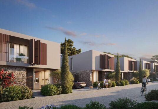 Property for sale Modern two-story houses, like Morea Coral Bay villas, with large windows and wooden shutters line a tree-lined street at sunset; people walk, a child bikes, and cars are parked in driveways surrounded by greenery. Presented by Palace Auctions