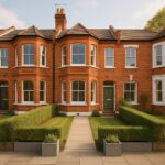 Property for sale Two red-brick terraced houses with bay windows and green doors, neatly trimmed hedges, small front lawns, and paved paths leading to each entrance—ideal as a 6-bedroom investment house in the heart of Wood Green on a sunny day. Presented by Palace Auctions