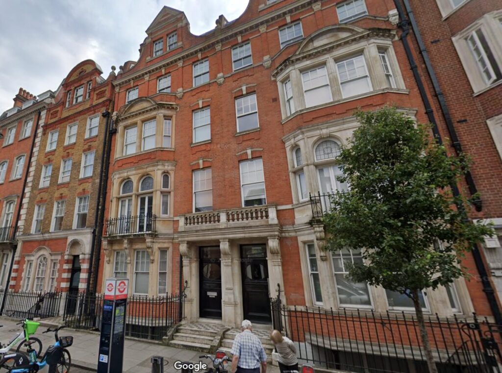 Property for sale A street view of ornate red-brick buildings with white stone details. Two people stand near bicycles on the sidewalk and a tree shades the entrance to this prime central London flat, a perfect 3-bedroom apartment in Marylebone W1G. Presented by Palace Auctions
