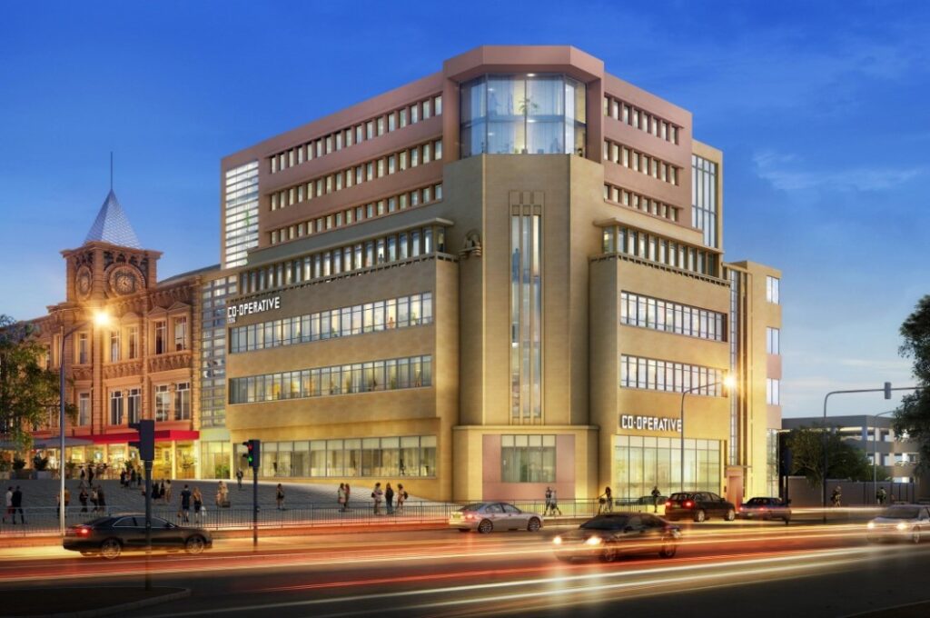 Property for sale A modern, multi-story office building with large windows and "CO-OPERATIVE" signs is illuminated at dusk in Huddersfield HD1, as cars pass by. To the left stands an ornate historic clock tower, near new 121-bed student accommodation Huddersfield offers. Presented by Palace Auctions