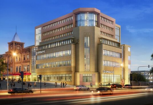 Property for sale A modern, multi-story office building with large windows and "CO-OPERATIVE" signs is illuminated at dusk in Huddersfield HD1, as cars pass by. To the left stands an ornate historic clock tower, near new 121-bed student accommodation Huddersfield offers. Presented by Palace Auctions