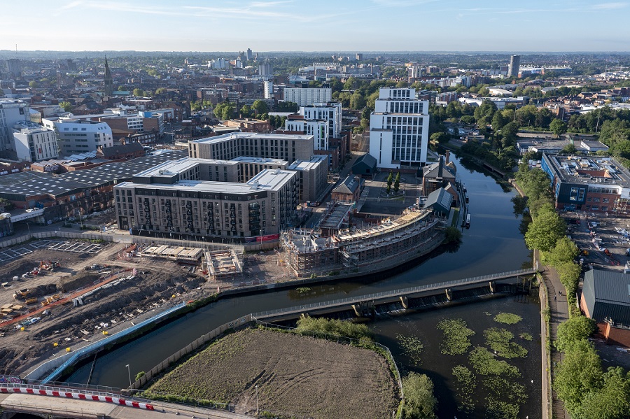 Property for sale Aerial view of a cityscape with modern buildings under construction beside a river, highlighted on City Regeneration Maps, surrounded by urban infrastructure, greenery, and clear blue sky in the background. Presented by Palace Auctions