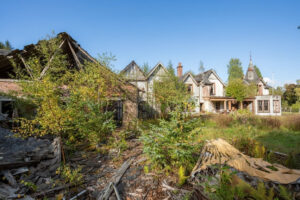 Property for sale An abandoned, overgrown property with decaying wooden buildings and collapsed roofs lies amid tall grass and trees under a clear blue sky, reminiscent of a forgotten Scottish manor house development. Presented by Palace Auctions