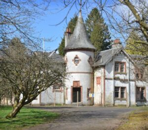 Property for sale A large, old stone house with a round turret and conical roof stands among leafless trees. This impressive Scottish manor house development features red-framed windows, weathered white walls, and is bordered by a paved driveway. Presented by Palace Auctions