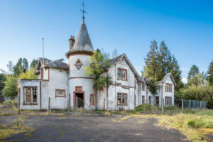 Property for sale An old, abandoned mansion with weathered white walls, broken windows, and a conical turret sits surrounded by overgrown vegetation—an intriguing site for a Scottish manor house development under the clear blue sky. Presented by Palace Auctions