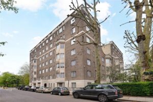 Property for sale A multi-storey brick Albion Gate apartment with white window frames on a tree-lined street in Central London W2, several parked cars along the curb, and blue sky with clouds above. Presented by Palace Auctions