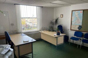 Property for sale A tidy office with two desks, blue chairs, a large window with vertical blinds, a potted plant, a whiteboard, and a wall map—ideal as a development or investment property for an upcoming Nottinghamshire auction. Sunlight brightens the room through the window. Presented by Palace Auctions