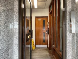 Property for sale A building entrance with a glass door, wooden internal doors, a yellow caution wet floor sign, granite walls, a wall-mounted entryphone, and a ceiling light—ideal for those seeking Mansfield Road property at a Nottinghamshire auction. Presented by Palace Auctions